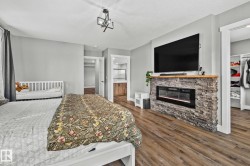 Bedroom with a walk in closet, dark wood-style floors, and a stone fireplace - 
