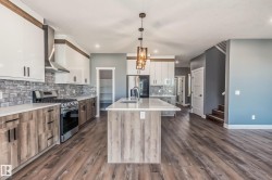 Kitchen with white cabinets, hanging light fixtures, appliances with stainless steel finishes, a kitchen island with sink, and wall chimney range hood - 