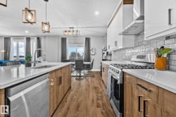 Kitchen featuring stainless steel appliances, brown cabinets, wall chimney range hood, tasteful backsplash, and hanging light fixtures - 