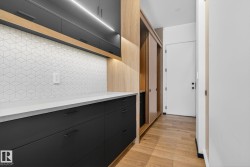 Kitchen featuring dark cabinets, modern cabinets, tasteful backsplash, light wood finished floors, and light stone counters - 