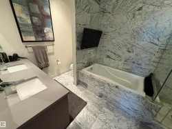 Bathroom with double vanity, a bath, and light marble finish flooring - 