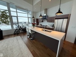 Kitchen with modern cabinets, stainless steel appliances, hanging light fixtures, a center island with sink, and a high ceiling - 