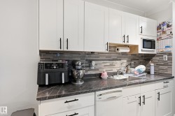 Kitchen featuring dark countertops, white appliances, white cabinetry, and backsplash - 