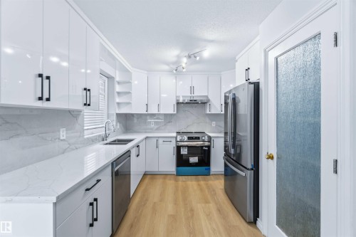 Kitchen with open shelves, stainless steel appliances, white cabinetry, light stone countertops, and a textured ceiling - 115 Deer Ridge Drive, St. Albert, AB - Indoor Photo Showing Kitchen With Double Sink With Upgraded Kitchen