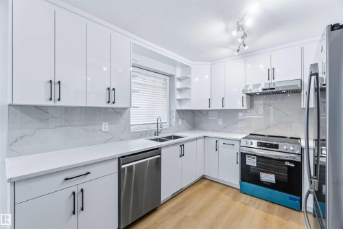 Kitchen featuring open shelves, appliances with stainless steel finishes, white cabinets, a textured ceiling, and light stone countertops - 115 Deer Ridge Drive, St. Albert, AB - Indoor Photo Showing Kitchen With Double Sink