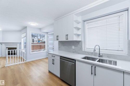 Kitchen featuring open shelves, dishwasher, white cabinets, light stone counters, and light wood finished floors - 115 Deer Ridge Drive, St. Albert, AB - Indoor Photo Showing Kitchen With Double Sink