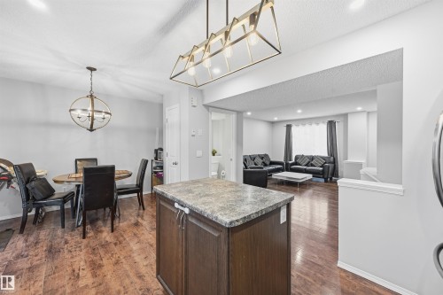 Kitchen featuring dark brown cabinets, pendant lighting, a kitchen island, a textured ceiling, and dark wood-type flooring - 21017 60 Avenue, Edmonton, AB - Indoor