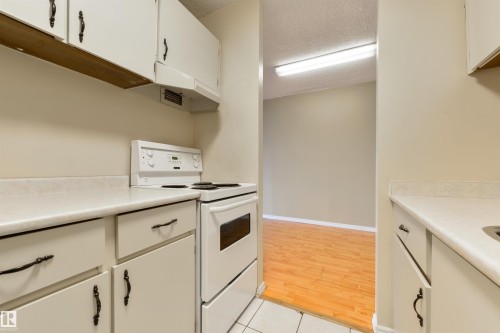 Kitchen featuring white electric range oven, light countertops, a textured ceiling, white cabinetry, and under cabinet range hood - 601 13910 Stony Plain Road, Edmonton, AB - Indoor Photo Showing Kitchen