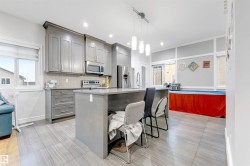 Kitchen with gray cabinets, a center island with sink, appliances with stainless steel finishes, light stone countertops, and a kitchen breakfast bar - 