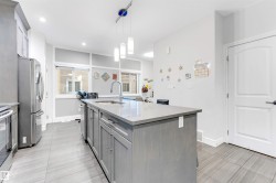 Kitchen with stainless steel appliances, pendant lighting, light stone counters, an island with sink, and gray cabinets - 