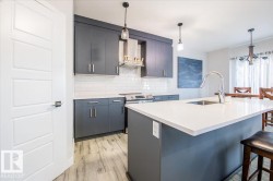 Kitchen with a kitchen bar, pendant lighting, wall chimney range hood, a center island with sink, and backsplash - 