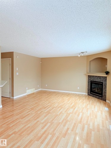 Unfurnished living room with a textured ceiling, a premium fireplace, and light wood-type flooring - 1711 37A Avenue, Edmonton, AB - Indoor With Fireplace
