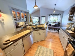 Kitchen featuring decorative light fixtures, stainless steel appliances, light wood-type flooring, vaulted ceiling, and glass insert cabinets - 