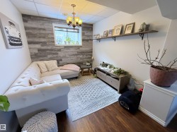 Living area featuring an accent wall, wooden walls, wood finished floors, a chandelier, and a paneled ceiling - 