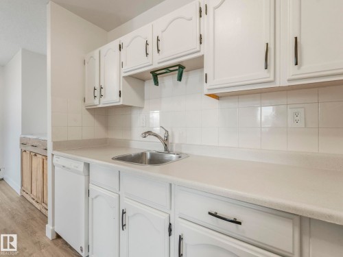 Kitchen featuring light countertops, decorative backsplash, dishwasher, white cabinetry, and light wood finished floors - 406 10125 109 Street, Edmonton, AB - Indoor Photo Showing Kitchen