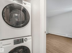 Laundry room with estacked washer and dryer, wood finished floors, and a baseboard heating unit - 