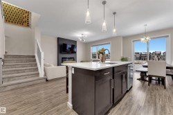 Kitchen featuring dark brown cabinetry, a chandelier, pendant lighting, open floor plan, and an island with sink - 