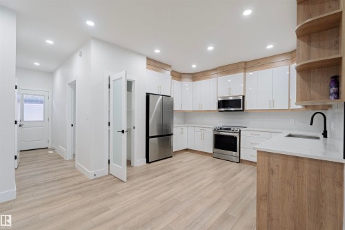 Kitchen with open shelves, appliances with stainless steel finishes, white cabinetry, light stone countertops, and light wood-style flooring - 244 Rolston Wynd, Leduc, AB - Indoor Photo Showing Kitchen