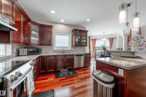 Kitchen with light stone counters, stainless steel appliances, hanging light fixtures, light wood-style flooring, and glass insert cabinets - 20524 58 Avenue, Edmonton, AB - Indoor Photo Showing Kitchen