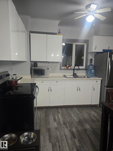 Kitchen with light countertops, stainless steel appliances, dark wood-style floors, white cabinets, and ceiling fan - 11516 88 Street, Edmonton, AB - Indoor Photo Showing Kitchen