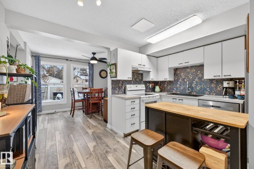 Kitchen featuring wood counters, a textured ceiling, white electric range oven, light wood-style floors, and white cabinetry - 7 Grandview Ridge, St. Albert, AB - Indoor Photo Showing Kitchen With Double Sink
