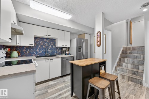 Kitchen with a breakfast bar, white cabinetry, butcher block countertops, a textured ceiling, and stainless steel appliances - 7 Grandview Ridge, St. Albert, AB - Indoor Photo Showing Kitchen