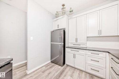 Kitchen featuring stainless steel appliances, white cabinets, light wood-type flooring, and dark stone counters - 507 11716 100 Avenue, Edmonton, AB - Indoor Photo Showing Kitchen