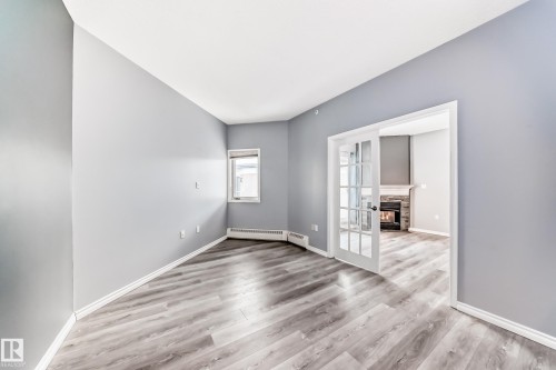 Empty room with light wood finished floors, a stone fireplace, and a baseboard radiator - 507 11716 100 Avenue, Edmonton, AB - Indoor Photo Showing Other Room