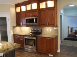 Kitchen featuring appliances with stainless steel finishes, decorative backsplash, dark stone counters, arched walkways, and glass insert cabinets - 