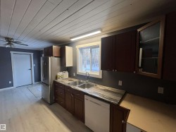 Kitchen with wood ceiling, light countertops, white dishwasher, dark brown cabinets, and light wood-style floors - 