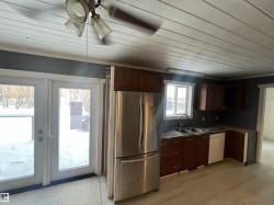 Kitchen featuring freestanding refrigerator, glass insert cabinets, white dishwasher, a ceiling fan, and dark countertops - 