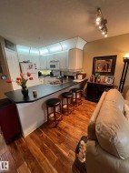Kitchen featuring dark countertops, a textured ceiling, a breakfast bar area, a peninsula, and white appliances - 