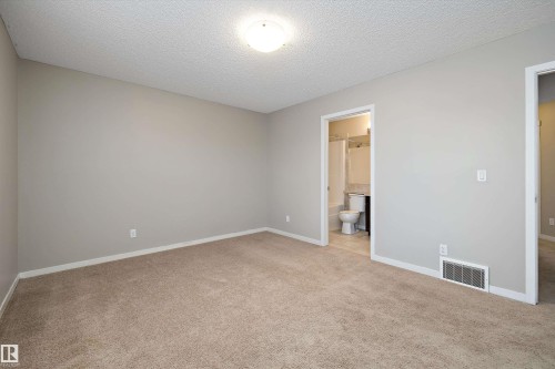 Unfurnished bedroom with light colored carpet, a textured ceiling, and ensuite bathroom - 5247 20 Avenue Sw, Edmonton, AB - Indoor Photo Showing Other Room
