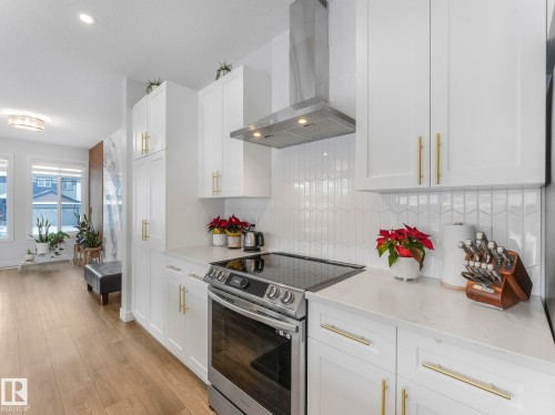Kitchen featuring wall chimney exhaust hood, stainless steel electric range oven, white cabinets, and light wood-style flooring - 4447 Kinsella Green, Edmonton, AB - Indoor Photo Showing Kitchen With Upgraded Kitchen
