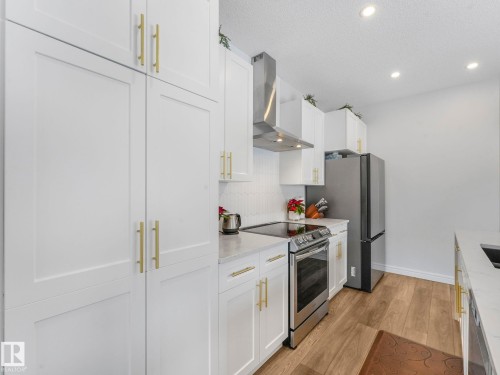 Kitchen with stainless steel electric range oven, wall chimney exhaust hood, light wood finished floors, white cabinetry, and a textured ceiling - 4447 Kinsella Green, Edmonton, AB - Indoor Photo Showing Kitchen With Upgraded Kitchen