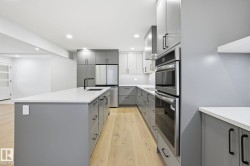 Kitchen with gray cabinetry, appliances with stainless steel finishes, light wood-type flooring, backsplash, and a center island with sink - 