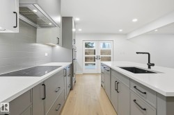 Kitchen with gray cabinetry, extractor fan, light wood-style floors, light stone counters, and black electric cooktop - 