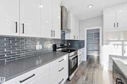 Kitchen with electric stove, dark stone counters, wall chimney exhaust hood, backsplash, and white cabinets - 