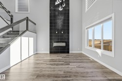 Unfurnished living room featuring a high ceiling, wood finished floors, stairs, and a tiled fireplace - 