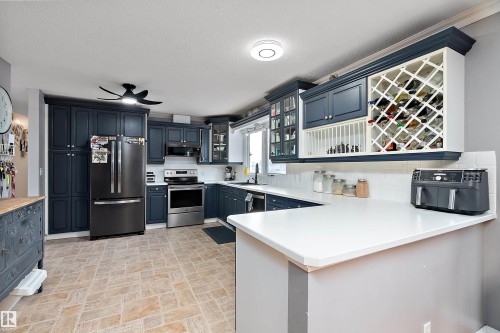 Kitchen featuring stainless steel appliances, glass insert cabinets, a peninsula, blue cabinetry, and tasteful backsplash - 145 Plum Crescent, Wetaskiwin, AB - Indoor Photo Showing Kitchen