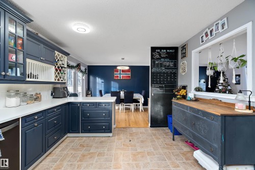 Kitchen with blue cabinets, stainless steel dishwasher, a peninsula, glass insert cabinets, and stone finish floors - 145 Plum Crescent, Wetaskiwin, AB - Indoor