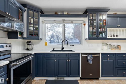 Kitchen with blue cabinets, glass insert cabinets, and stainless steel appliances - 145 Plum Crescent, Wetaskiwin, AB - Indoor Photo Showing Kitchen With Double Sink
