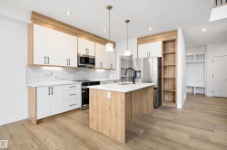 Kitchen with decorative light fixtures, white cabinets, a kitchen island with sink, appliances with stainless steel finishes, and light wood-style flooring - 