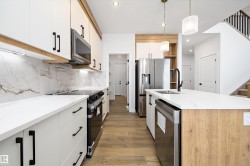 Kitchen featuring light stone counters, appliances with stainless steel finishes, hanging light fixtures, light wood-type flooring, and backsplash - 