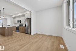 Kitchen with white cabinetry, stainless steel appliances, brown cabinets, light wood-style flooring, and hanging light fixtures - 