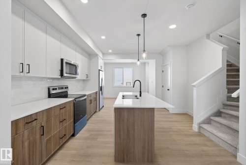 Kitchen featuring brown cabinetry, stainless steel appliances, white cabinetry, modern cabinets, and an island with sink - 119 Brickyard Drive, Stony Plain, AB - Indoor Photo Showing Kitchen With Double Sink With Upgraded Kitchen