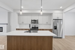 Kitchen with decorative backsplash, white cabinets, stainless steel appliances, pendant lighting, and a center island with sink - 