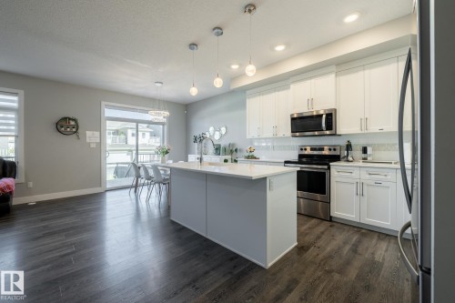 Kitchen featuring appliances with stainless steel finishes, backsplash, white cabinetry, a kitchen island with sink, and a textured ceiling - 1440 Darby Green, Edmonton, AB - Indoor Photo Showing Kitchen With Upgraded Kitchen