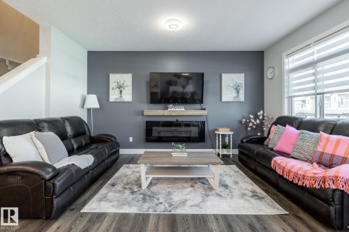 Living area with wood finished floors, a textured ceiling, and a glass covered fireplace - 1440 Darby Green, Edmonton, AB - Indoor Photo Showing Living Room With Fireplace