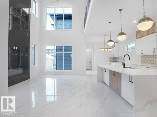 Kitchen featuring white cabinetry, light stone countertops, decorative light fixtures, decorative backsplash, and an island with sink - 6131 Crawford Drive, Edmonton, AB - Indoor Photo Showing Kitchen With Upgraded Kitchen